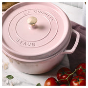 Staub | Round Dutch Oven, Pink Peony, 5.5 QT, with brass knob, on marble countertop, surrounded by garlic, basil, and vine tomatoes, embodying elegant kitchenware from Athens Cooks.