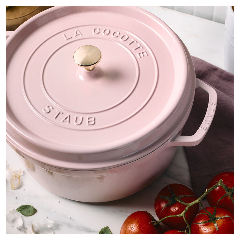 Staub | Round Dutch Oven, Pink Peony, 5.5 QT, with brass knob, on marble countertop, surrounded by garlic, basil, and vine tomatoes, embodying elegant kitchenware from Athens Cooks.