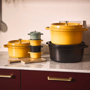 Staub | Mini Round Dutch Oven, Citron, 0.275 QT., sits among enameled cookware on a marble countertop, showcasing its compact, versatile design for flavorful, single-serve dishes.
