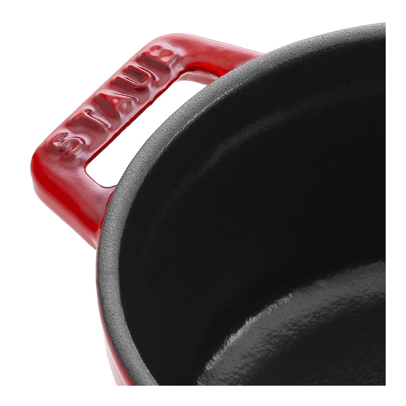 Close-up of the red Staub | Mini Round Dutch Oven, Cherry, 0.275 QT., highlighting its enameled cast-iron rim and handle with the STAUB logo embossed.