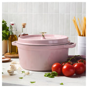 Staub Round Dutch Oven, Pink Peony, 7 QT, on a kitchen countertop with tomatoes, garlic, basil, olive oil, and spaghetti, set against a tiled backsplash.