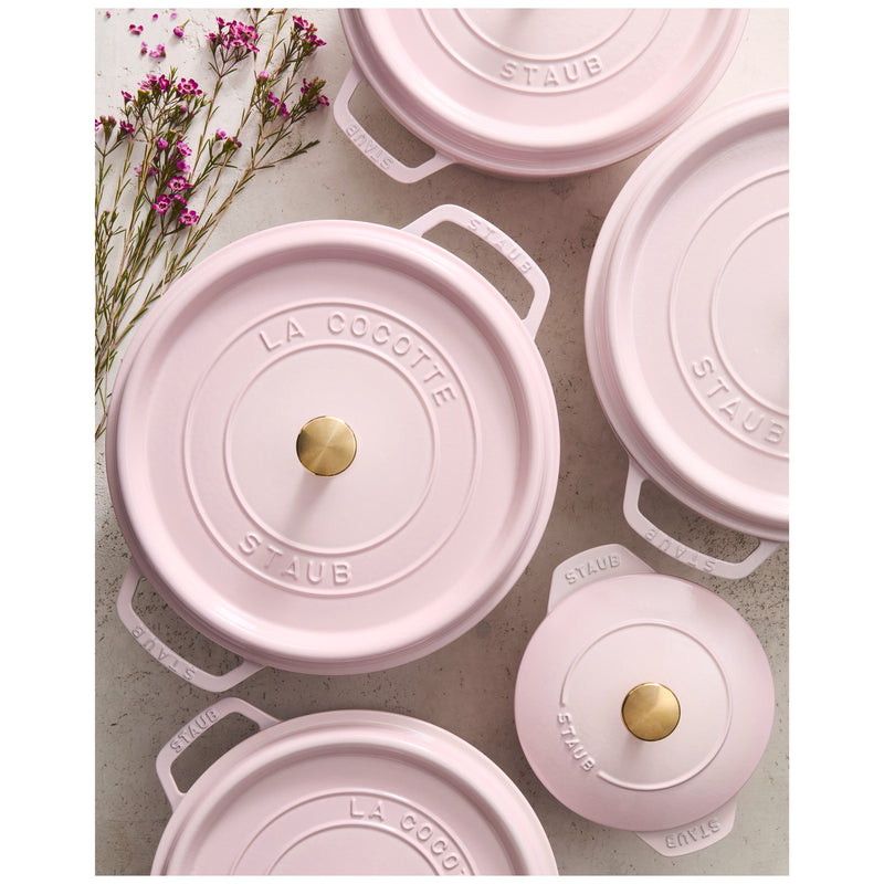 Overhead view of Staub Round Dutch Oven, Pink Peony, 7 QT, featuring enameled cast-iron pots with brass knobs and embossed lids, accented by delicate pink flowers.