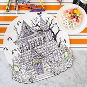Hester & Cook | Haunted House Coloring Placemat on a countertop, partially colored with crayons, accompanied by a plate of candied popcorn and yogurt-covered pretzels.