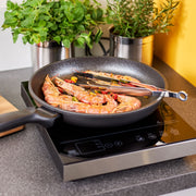 Rösle | Fine Tongs W Silicone Tips 9 Inches resting on a skillet with prawns and chilies on an induction cooktop, ideal for precise and safe cooking.