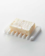 Yamazaki Home | Flow Self-Draining Soap Tray: Off-white bar soap with flecks on a black silicone tray, featuring raised ridges for effective drainage and drying.