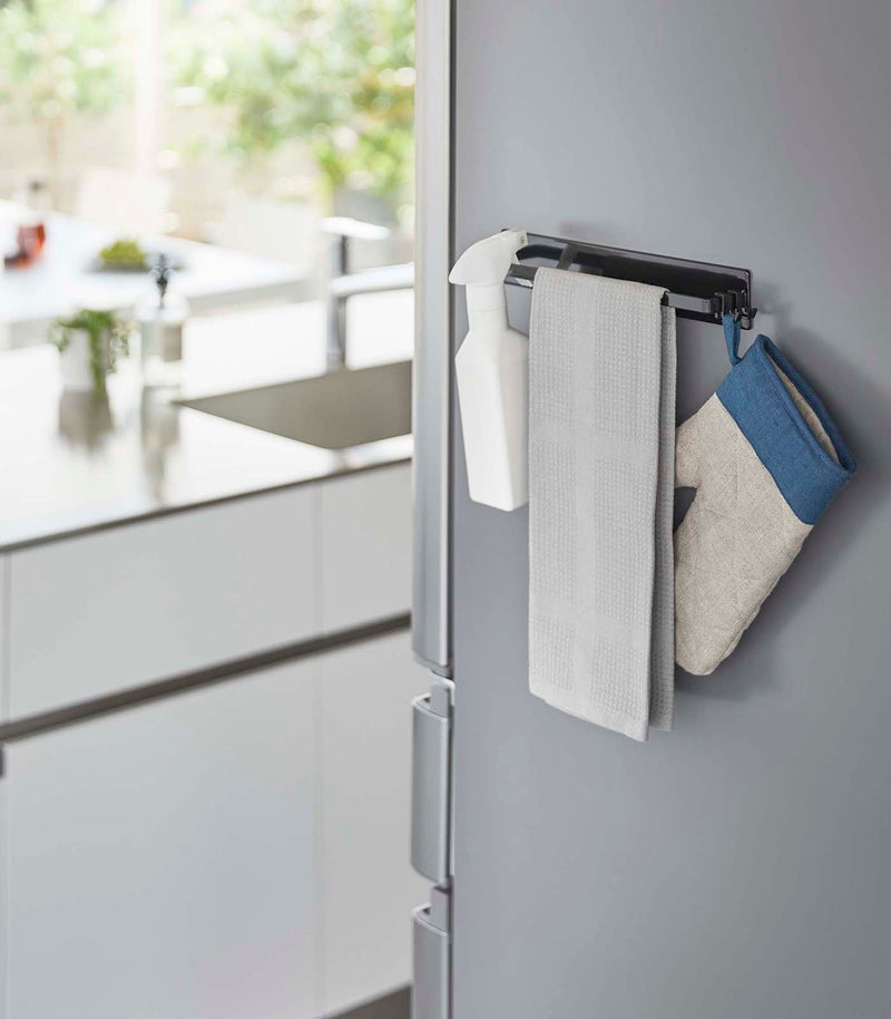 Yamazaki Home | Magnetic Kitchen Towel Hanger, Steel, White, holding a spray bottle, dish towel, and oven mitt on a modern fridge for convenient kitchen organization.