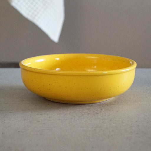 La Gabbianella | Pisa, Pasta/Soup Bowl, Yellow: A simple yellow ceramic bowl, perfect for serving fruit salads, sits on a neutral surface, partially framed by a white cloth.