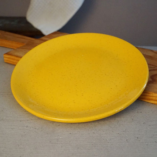 La Gabbianella | Pisa, Dinner Plate, Yellow: A handmade, speckled yellow ceramic plate, crafted in Italy, showcased on a countertop, embodying quality kitchenware from Athens Cooks.
