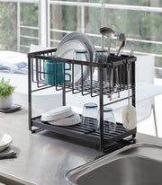 Yamazaki Home | Two-Tier Dish Rack, White, on a countertop, loaded with plates, glasses, a mug, utensils, and features a 360-degree rotating draining spout.