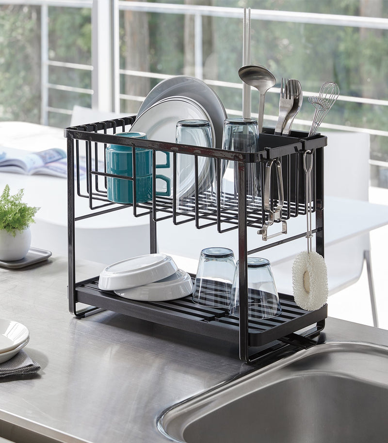 Yamazaki Home | Two-Tier Dish Rack, White, on a countertop, loaded with plates, glasses, a mug, utensils, and features a 360-degree rotating draining spout.