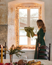 MagicLinen | Linen Decorative Bow, Forest Green, adorns a window in a cozy holiday dining nook, adding a festive touch with its elegant, lightweight design.