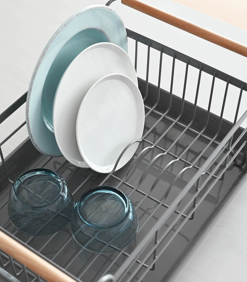 Yamazaki Home | Steel + Wood Dish Rack with Drainer Spout, showcasing plates and bowls, features wooden handles and a removable drip tray for stylish kitchen organization.