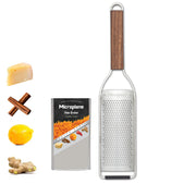Microplane | Master Series Fine Grater with Walnut Handle, featuring a stainless-steel surface and protective cover, alongside cheese, cinnamon, lemon, and ginger for zesting.