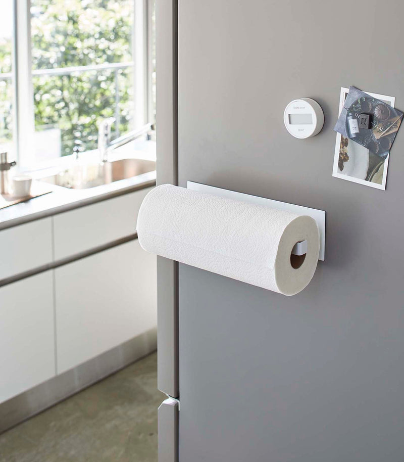 Yamazaki Home's white magnetic paper towel holder on a gray fridge, keeping the kitchen organized with postcards and a digital timer magnet.