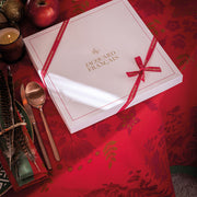 Le Jacquard Francais Féerie Tablecloth, Red, 69 x 98, elegantly displayed with festive decor, including a gift box, enhancing a holiday table setting.