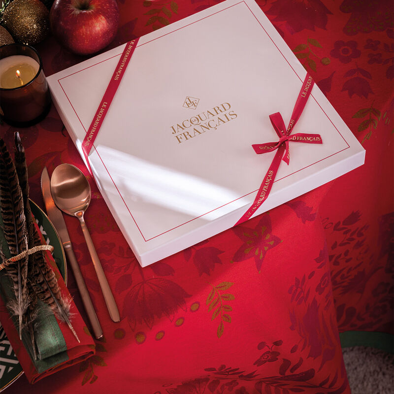 Le Jacquard Francais Féerie Tablecloth, Red, 69 x 98, elegantly displayed with festive decor, including a gift box, enhancing a holiday table setting.