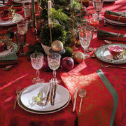 Le Jacquard Francais Féerie Tablecloth in red elegantly sets a festive table with gold flatware, crystal goblets, and a lush evergreen centerpiece.