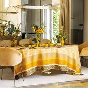 Le Jacquard Francais Gipsy Tablecloth in yellow adorns an oval dining table with sunflowers, lemons, and amber glasses, creating a vibrant, summery tablescape.