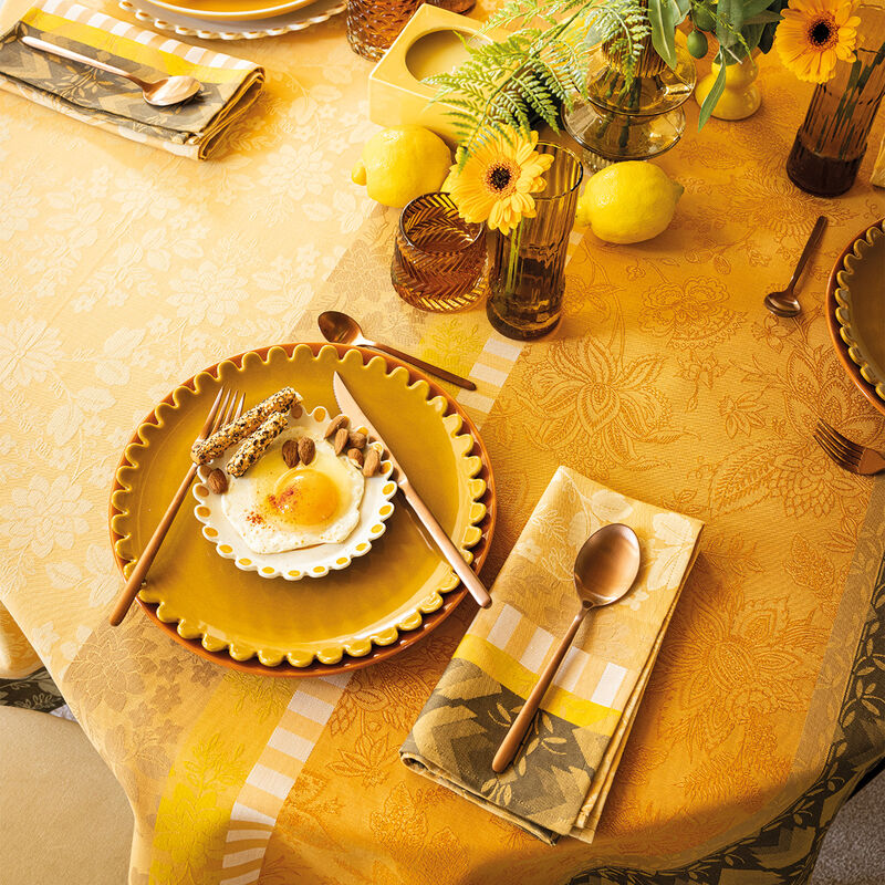 Le Jacquard Francais | Gipsy Tablecloth in yellow supports a brunch setting with floral motifs, copper flatware, amber glasses, and lemons, evoking a bohemian, global ambiance.