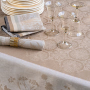 Le Jacquard Francais Bucolique Tablecloth in beige, elegantly draped on a table with a rolled napkin, plates, and wine glasses, creating a refined dining atmosphere.