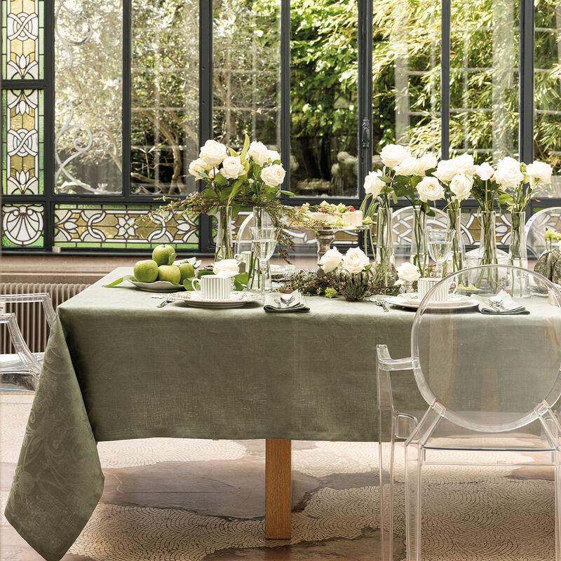 Elegant dining setup featuring Le Jacquard Francais Tivoli Tablecloth in green, adorned with white roses, green apples, and delicate pastries.