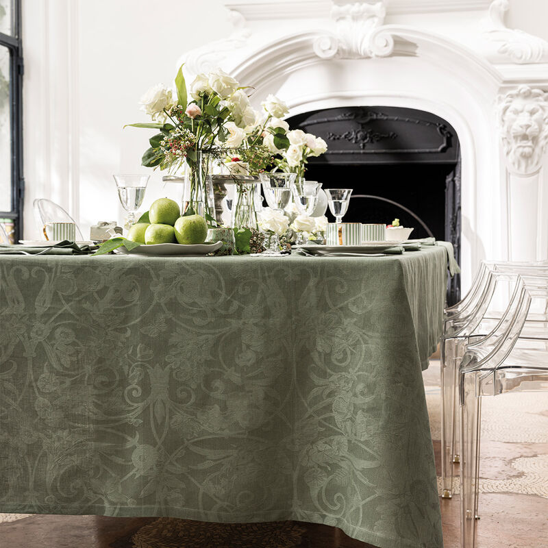 Le Jacquard Francais | Tivoli Tablecloth, Green, elegantly drapes a dining table, adorned with green apples, floral vases, crystal glasses, and pristine dinnerware.