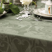 Le Jacquard Francais Tivoli Tablecloth in green with floral-scroll pattern, elegantly set with a teacup, fork, and rose, enhancing any dining experience.