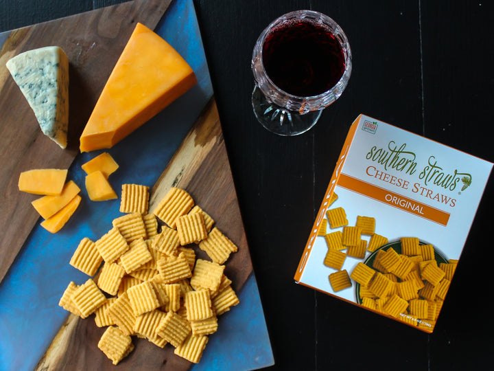 Southern Straws Cheese Straws arranged with cheddar, blue cheese, crackers, and red wine on a wooden board, showcasing a classic Southern snack spread from Athens Cooks.