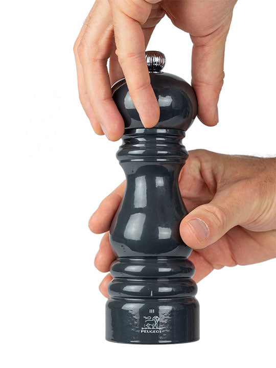 Hands using the Peugeot | Paris u'Select Wooden Pepper Mill in Slate Gloss, 7 inches, showcasing its elegant design and precise grind adjustment feature.