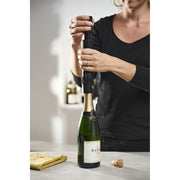 Woman using Peugeot Preserve Champagne Stopper to open champagne bottle, showcasing its functionality as an essential barware tool from Athens Cooks.