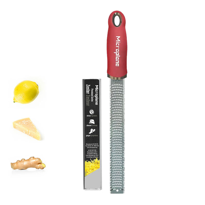 Microplane Premium Zester, Grater - Pomegranate Red with packaging, shown beside a lemon, cheese wedge, and ginger, ideal for precise zesting and grating.