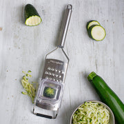 Microplane | Professional Series Extra Coarse Cheese Grater on wood surface with grated zucchini, showcasing its stainless-steel design and functionality for efficient meal preparation.