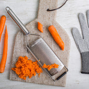 Microplane | Professional Series Fine Grater on stone board with carrots, grated shavings, and cut-resistant glove, showcasing its precision and durability for culinary use.