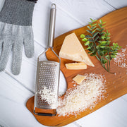 Microplane Professional Series Coarse Grater on a wooden board with grated cheese, protective glove, and cheese wedge; showcases precision grating for culinary excellence.