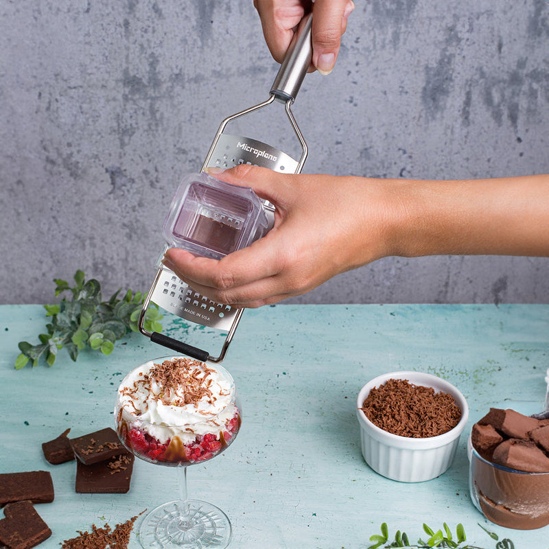 Close-up of the Microplane Professional Series Coarse Grater shaving chocolate over a dessert, highlighting its sharp efficiency and ergonomic design in a culinary setting.