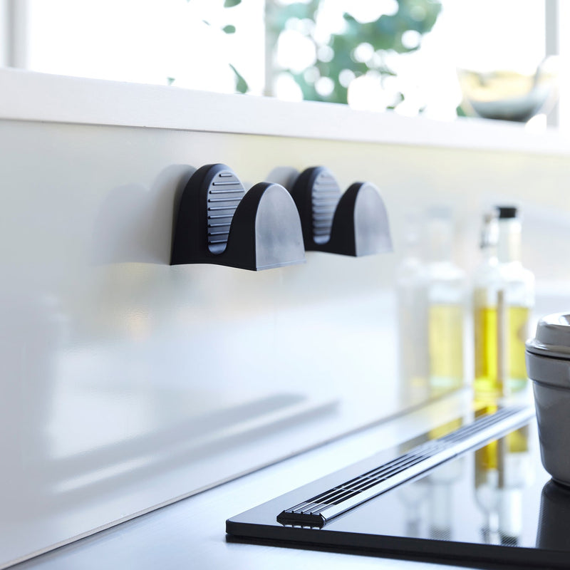 Yamazaki Home's Magnetic Pot Holders in black, mounted on a kitchen wall, offer a sleek, modern solution for effortlessly handling hot cookware.
