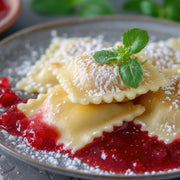Marcato Ravioli Tablet displayed with dessert ravioli in fruit sauce, garnished with powdered sugar and herbs, showcasing its capability to create perfect sweet or savory pasta.