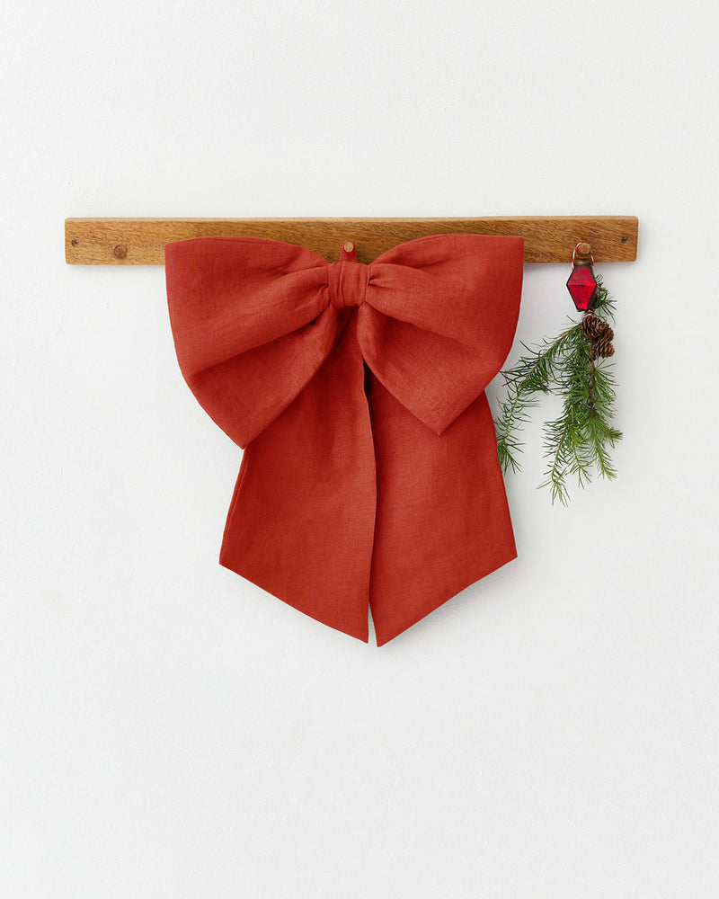 MagicLinen | Linen Decorative Bow, Red: A rust-red linen bow with a pine sprig and red ornament, perfect for festive decorating on walls or doors.