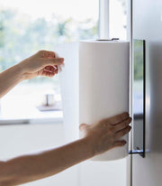 Yamazaki Home | Magnetic Steel Paper Towel Holder, White, mounted on a fridge, with hands pulling a sheet, showcasing its space-saving design in a modern kitchen.