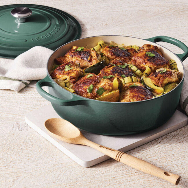 Le Creuset Signature Round Wide Oven - Meringue filled with browned chicken and squash, on a board with a spoon and lid, showcasing versatile cooking elegance.