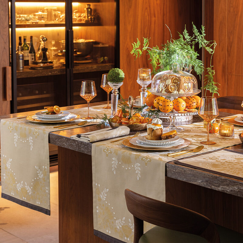Festive dining table with Le Jacquard Francais | Féerie Napkin, Yellow, amid elegant settings, amber glassware, and a citrus-clove centerpiece, creating a warm, inviting holiday ambiance.