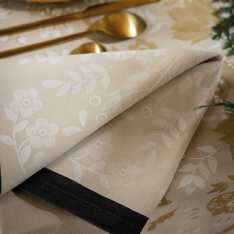 Le Jacquard Francais | Féerie Napkin, Yellow, elegantly folded with white floral motifs, accompanied by gold-tone spoons and greenery, evokes festive charm with its folkloric Christmas design.