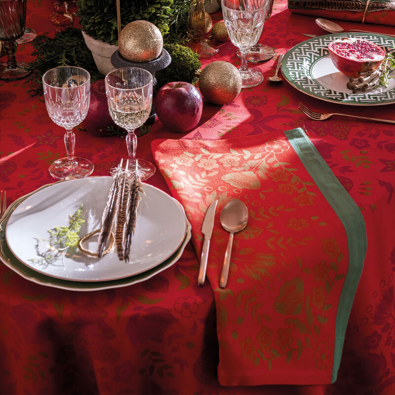 Festive table featuring Le Jacquard Francais | Féerie Napkin, Red, with decorative feathers, greenery, and elegant cutlery, embodying a folkloric Christmas ambiance.