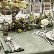 Elegant tablescape showcasing a Le Jacquard Francais Tivoli Napkin in green, paired with silverware, mini cakes, and floral accents for a sophisticated dining experience.