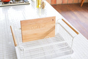 Yamazaki Home | Steel + Wood Dish Rack with Drainer Spout, featuring a sleek steel frame, wooden handles, and a cutting board in a modern kitchen setting.