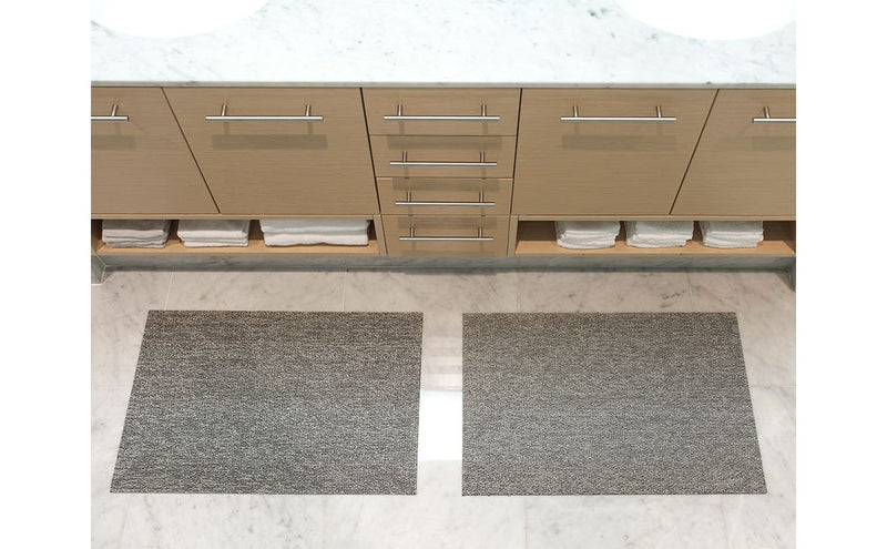Chilewich | Heathered Shag Mats in Grey, 24 x 36, on a bathroom counter with two rugs, combining durability with a plush look for versatile home use.
