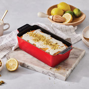 Le Creuset | Signature Loaf Pan - Sea Salt with lemon loaf cake topped with glaze and pistachios, surrounded by lemons, pistachios, and baking tools on a marble board.