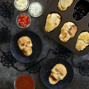 Nordic Ware Skull Cakelet Pans display baked skull-shaped pockets with cheese, onions, tomatoes, and sauce, ideal for Halloween-themed snacks or desserts.