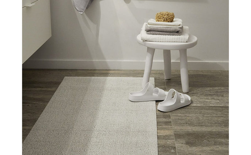 Chilewich Solid Shag Mat in Snow, 24 x 36, showcased on a wooden floor with towels and sandals, ideal for indoor or outdoor use.