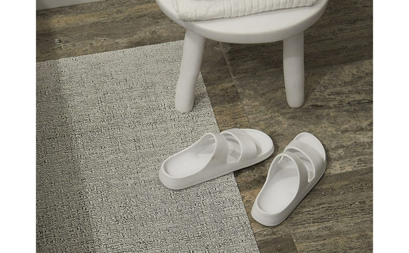 Chilewich Solid Shag Mats - Snow, 24 x 36, displayed on a rug next to white sandals, showcasing its indoor use and contemporary design.